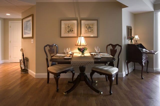 A cozy dining room with a wooden table set for four, adorned with a central lamp and artwork on the walls.
