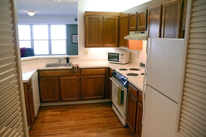A cozy kitchen featuring wooden cabinets, a fridge, oven, microwave, and a sink.