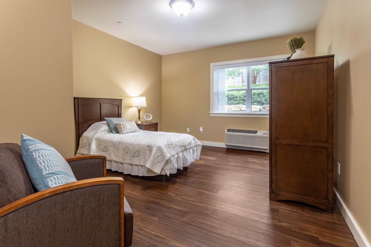 A cozy bedroom with a single bed, armchair, and wooden flooring.