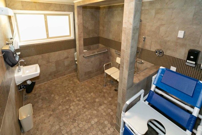A spacious, wheelchair-accessible bathroom equipped with handrails and a shower chair.