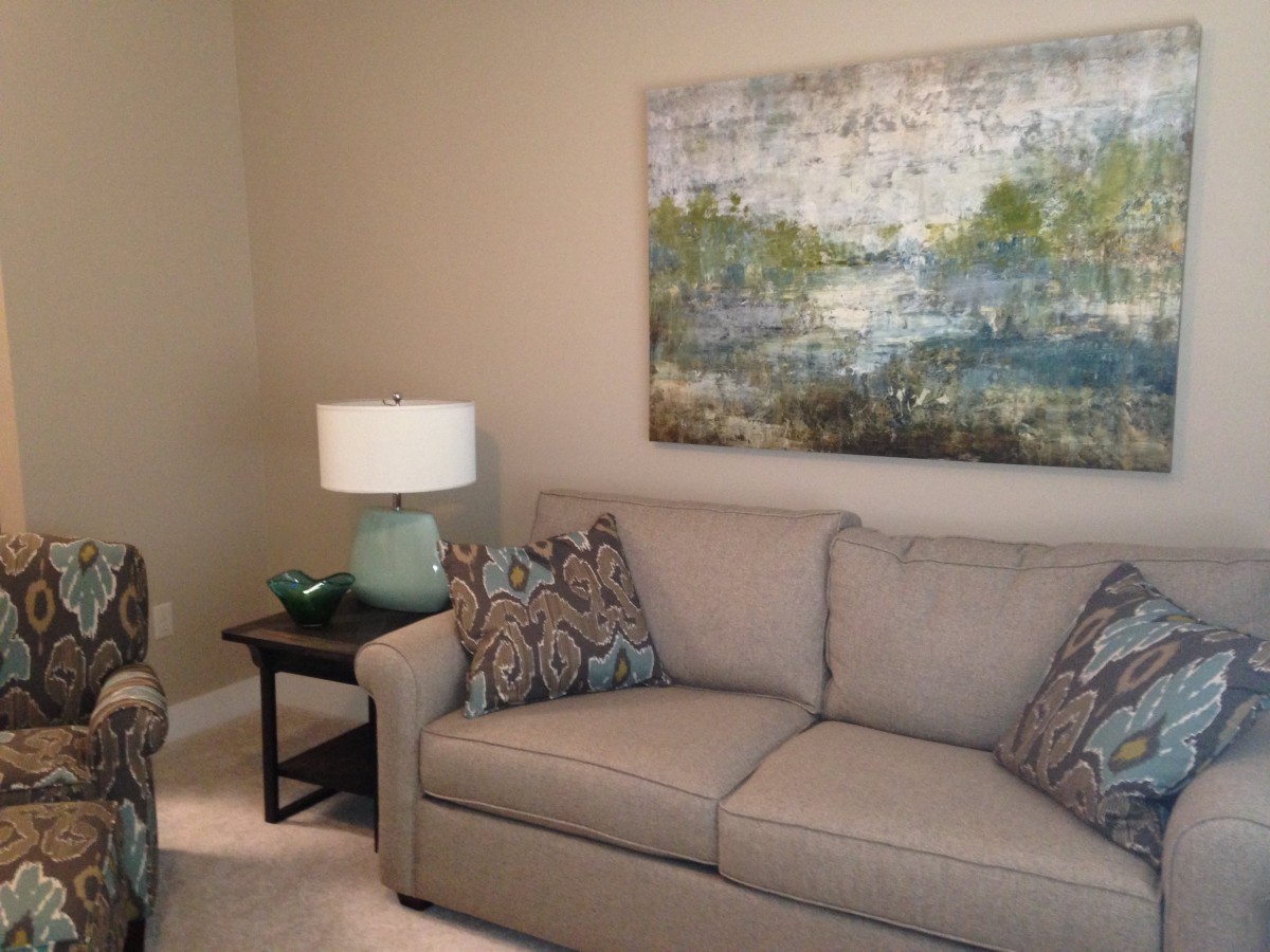 A cozy living room with a beige sofa, decorative pillows, a side table with a lamp, and abstract artwork on the wall.