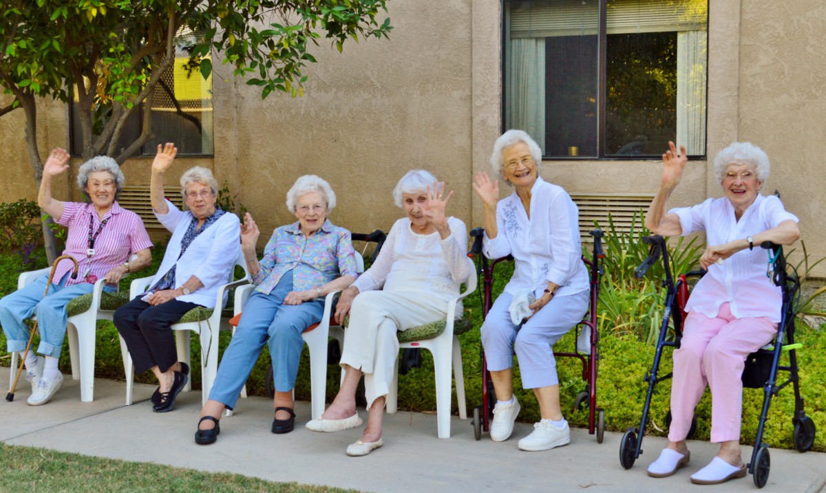 A group of elderly women sitting outdoors, waving and enjoying the day.