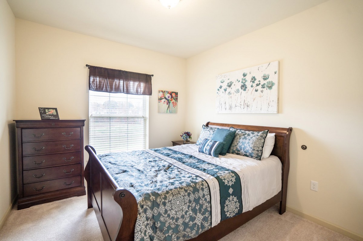 A cozy bedroom with a wooden bed frame, decorated with blue and white bedding, complemented by artwork on the walls.
