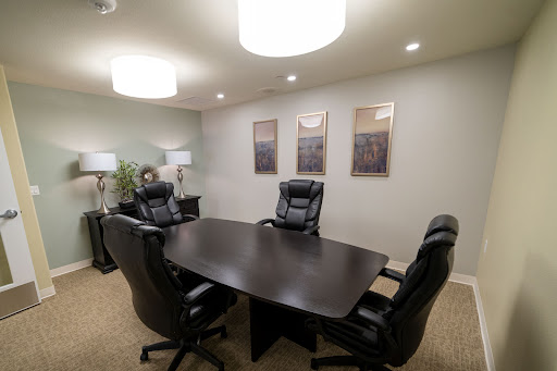 A modern conference room featuring a dark wooden table surrounded by black leather chairs, illuminated by stylish overhead lights.