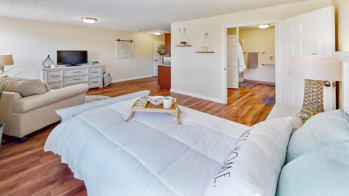 A modern and cozy bedroom with wooden flooring, featuring a bed with a tray, television, and stylish decor.