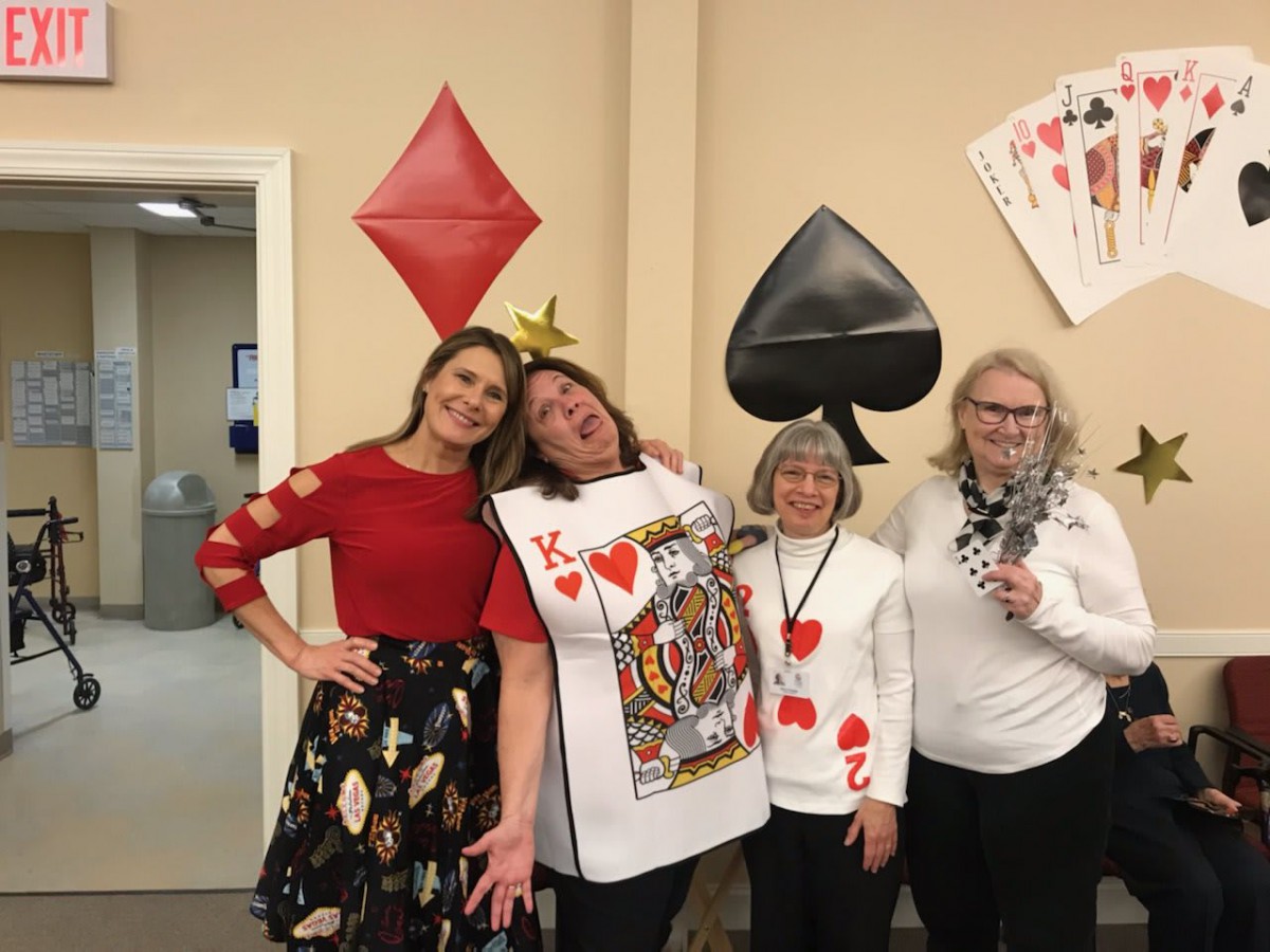 A group of people dressed in playing card-themed costumes, posing in front of a wall decorated with large card symbols.