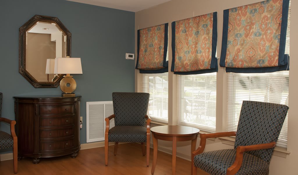 A cozy living room corner with two chairs, a small table, and window blinds.