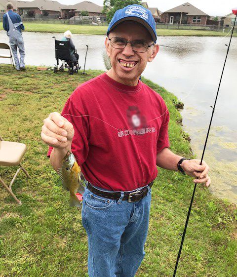 A person smiles while holding a small fish caught by the lake.