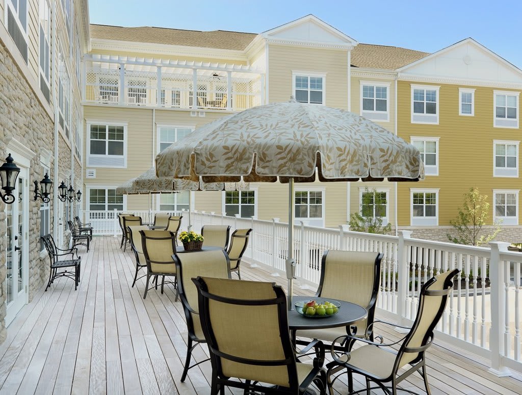 A sunny outdoor patio area with tables, chairs, and umbrellas in front of a building.