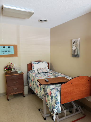 A cozy hospital room featuring a single bed with floral bedding, complemented by a nightstand and decorative wall art.