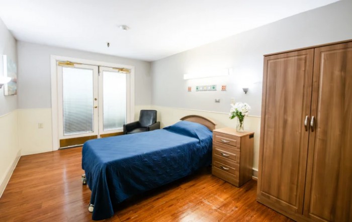 A minimalist bedroom with a single bed, wooden flooring, and simple furniture.