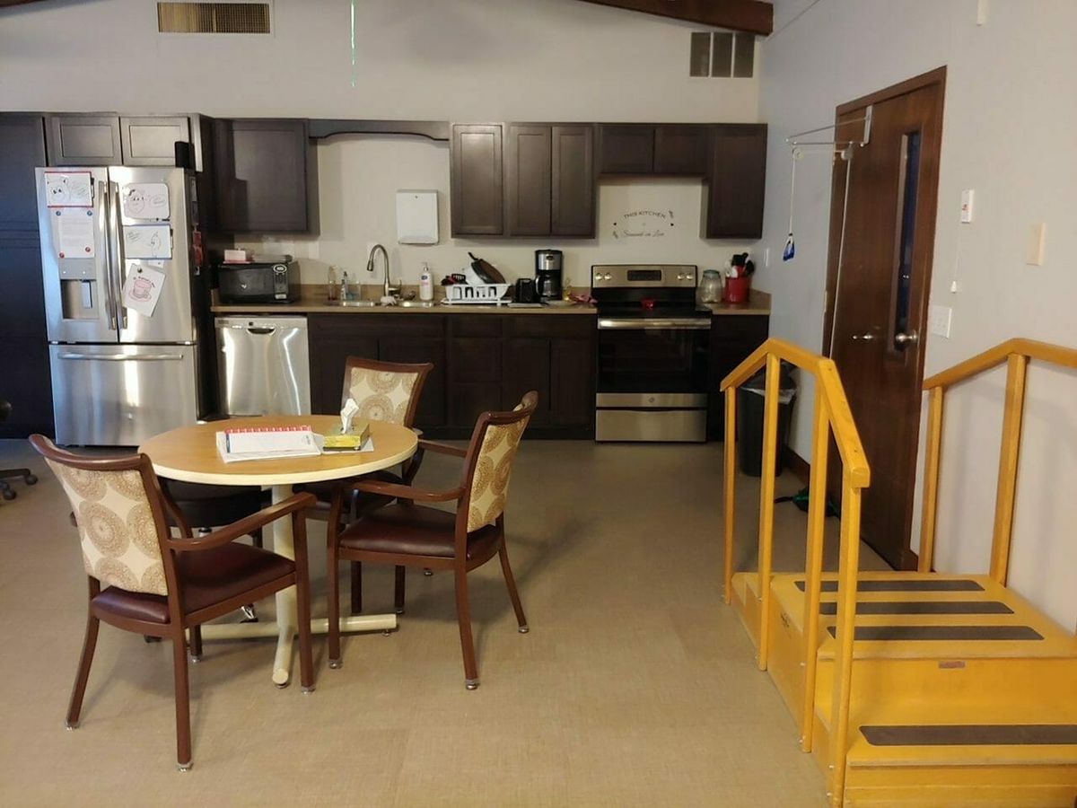 A cozy kitchen and dining area featuring a small round table, chairs, and indoor stairs near modern appliances.