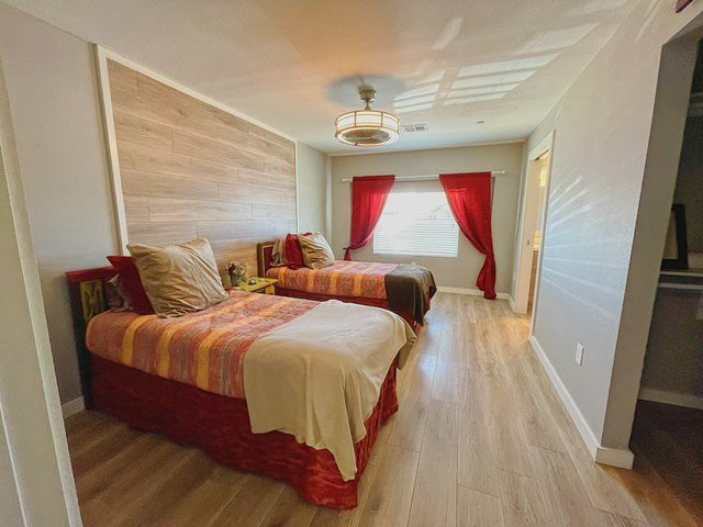 A cozy bedroom with twin beds, red curtains, and wood flooring.