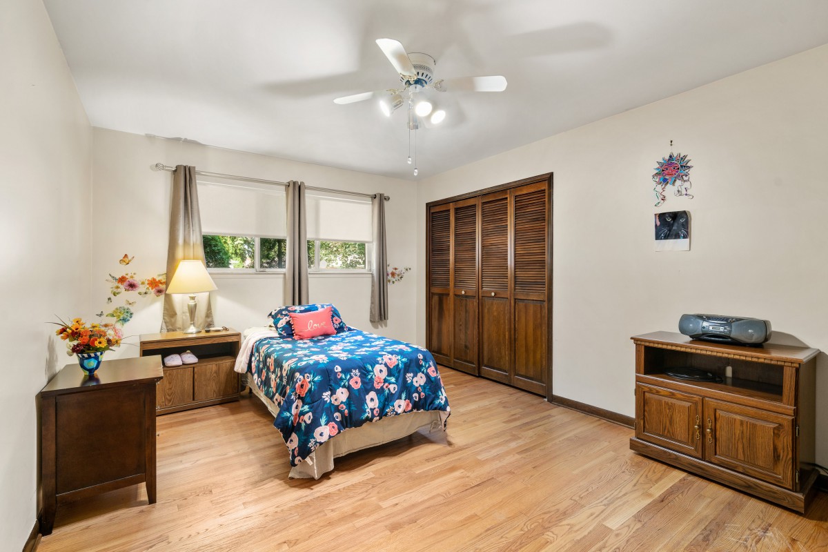 A cozy bedroom with a single bed, wooden flooring, and a ceiling fan.