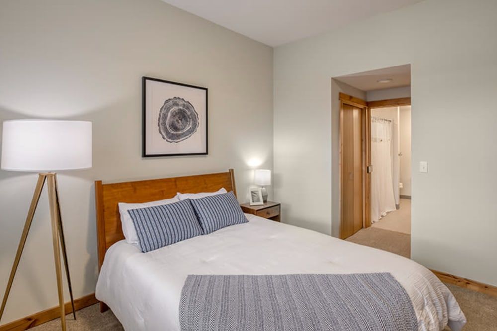 A cozy bedroom with a neatly made bed, wall art, and a bedside lamp.