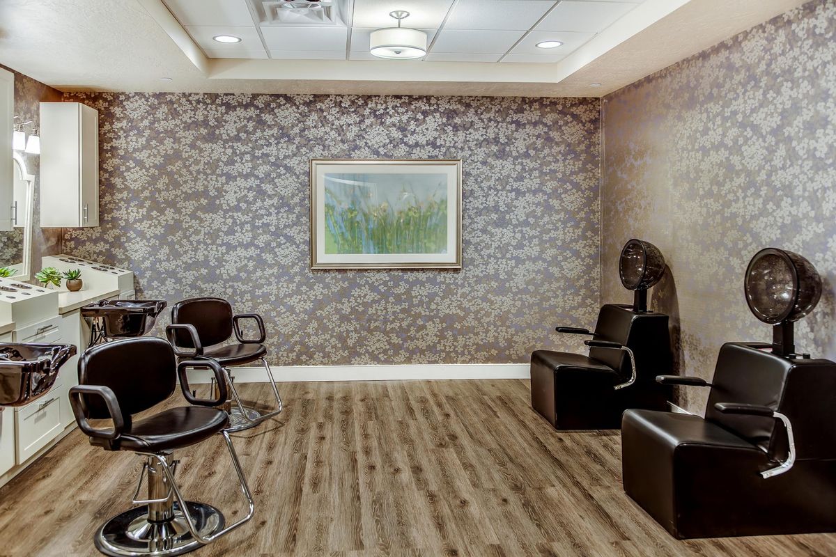 A modern salon interior with stylish chairs, a hair dryer, and floral wallpaper.