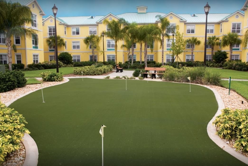 A hotel courtyard featuring a putting green surrounded by palm trees and a yellow building in the background.