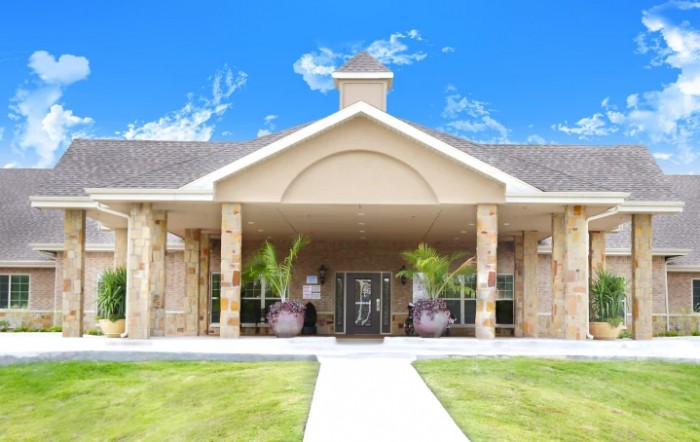 A welcoming building entrance with a well-maintained lawn and clear blue sky.