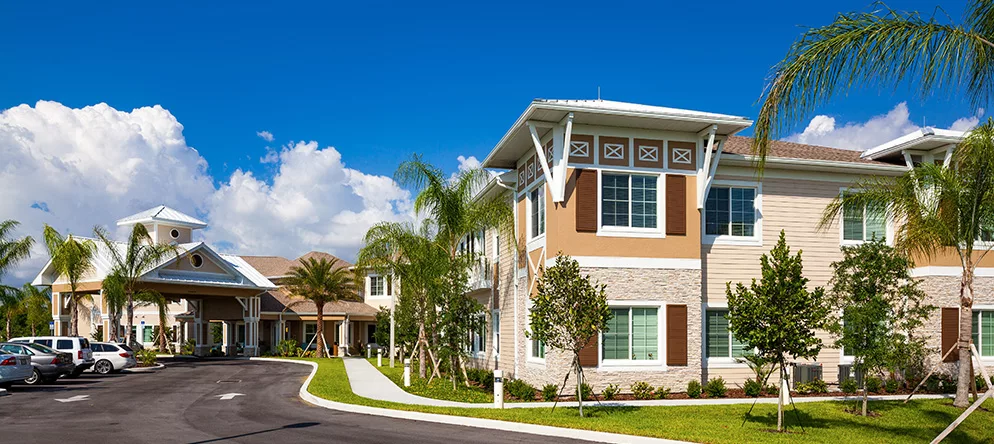A modern residential building surrounded by palm trees and lush landscaping under a clear blue sky.