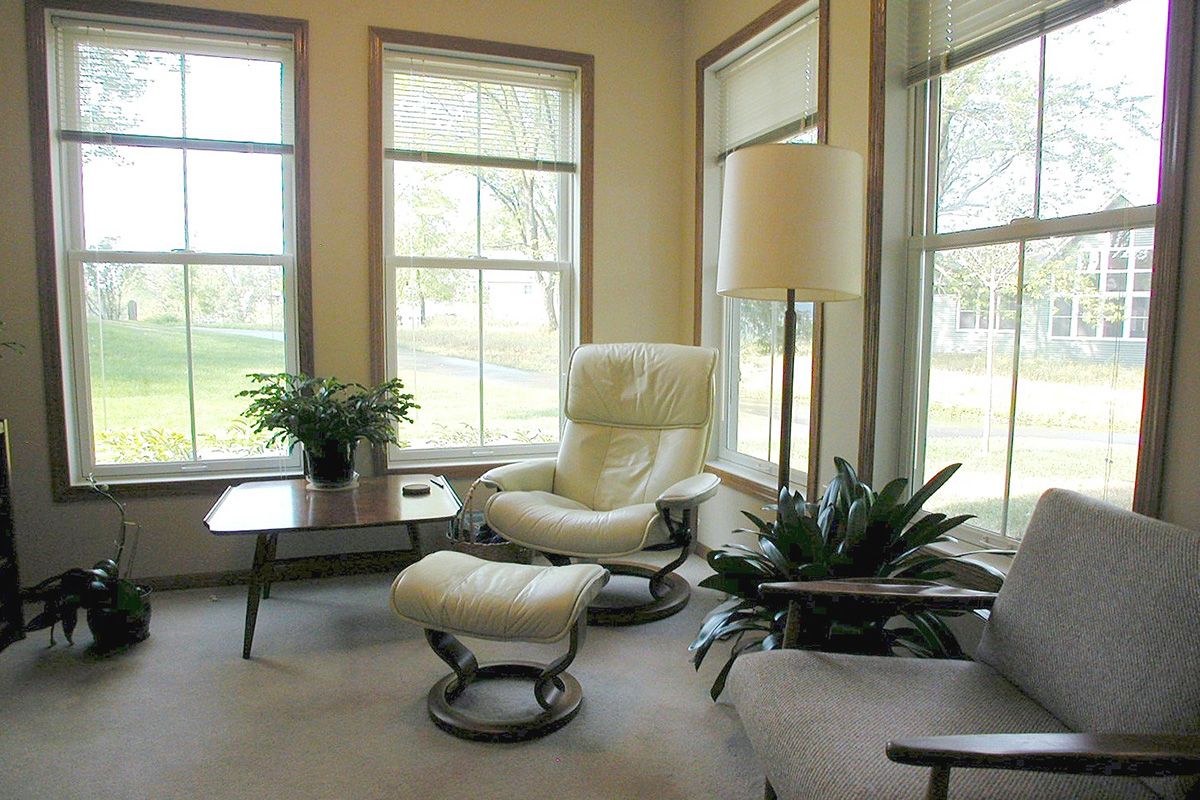 A cozy living room corner with a white armchair, footstool, and large windows.