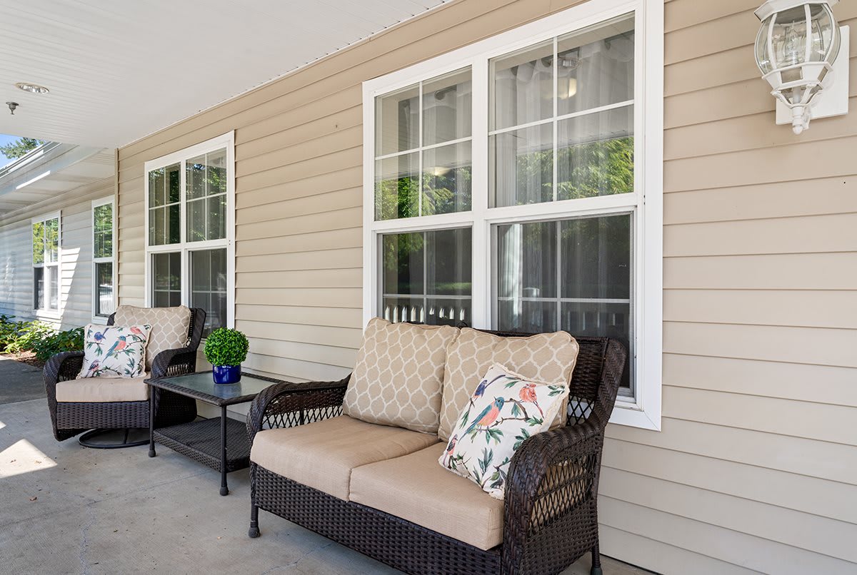 A cozy porch area with wicker couches and decorative cushions alongside windows.