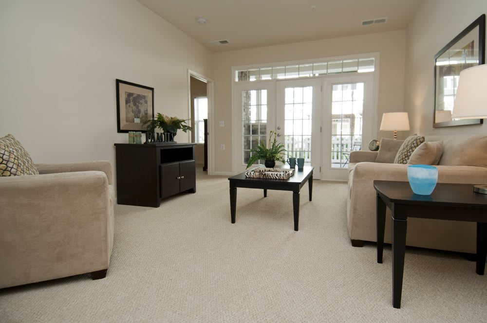 A cozy living room with neutral tones, featuring a sofa, coffee table, and large windows allowing natural light.