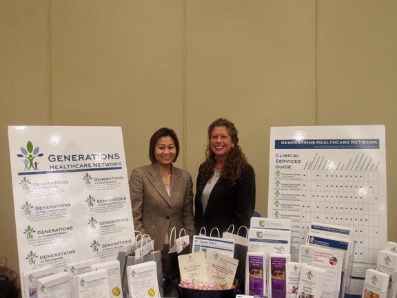 Two women standing at a conference booth displaying various informational materials.