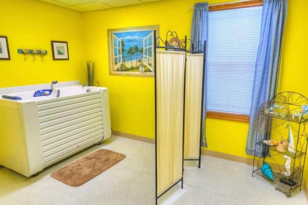 A cozy spa room with bright yellow walls, featuring a massage table and a partition screen for privacy.