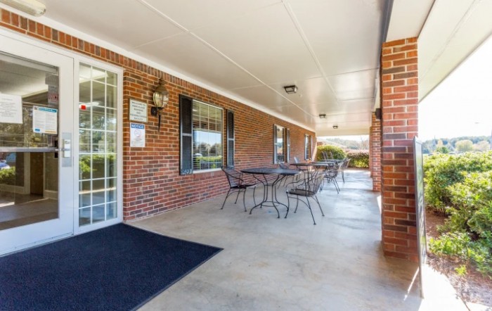 A covered outdoor patio with tables and chairs adjacent to a brick building.