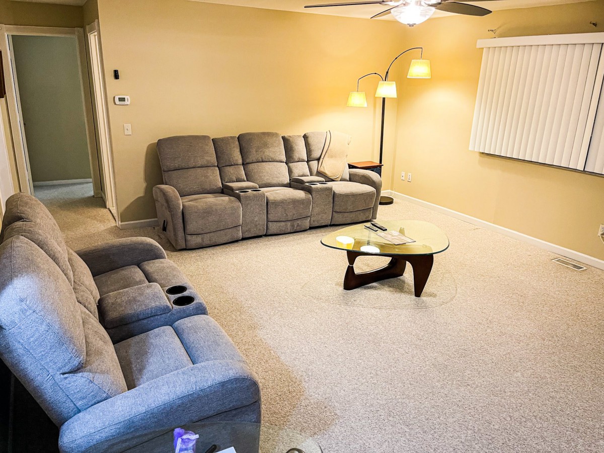 A cozy living room with a comfortable sectional sofa, a unique glass coffee table, and warm lighting from floor and ceiling lamps.