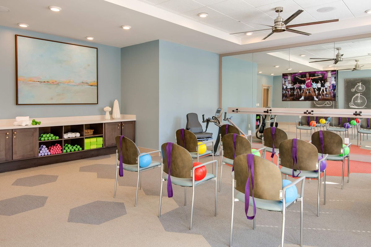A modern exercise room featuring chairs, yoga balls, and gym equipment set against a backdrop of mirrors.