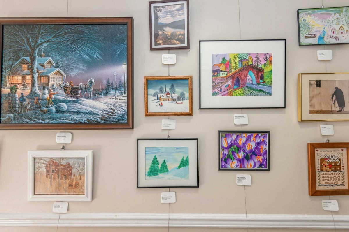 A wall display of various framed paintings in an art gallery, showcasing diverse artistic styles and subjects.