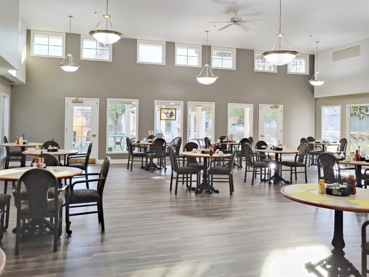 A spacious dining area with multiple tables and chairs, featuring large windows and ceiling lights.