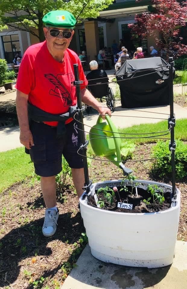 A person watering plants in a garden using a green watering can.
