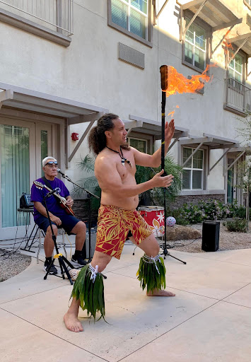 A vibrant fire dancer showcases traditional Hawaiian performance skills, while a musician provides lively accompaniment in the background.