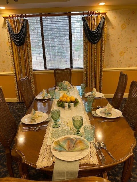 A beautifully set dining table with elegant plates, glassware, and a fruit centerpiece in a formal dining room.