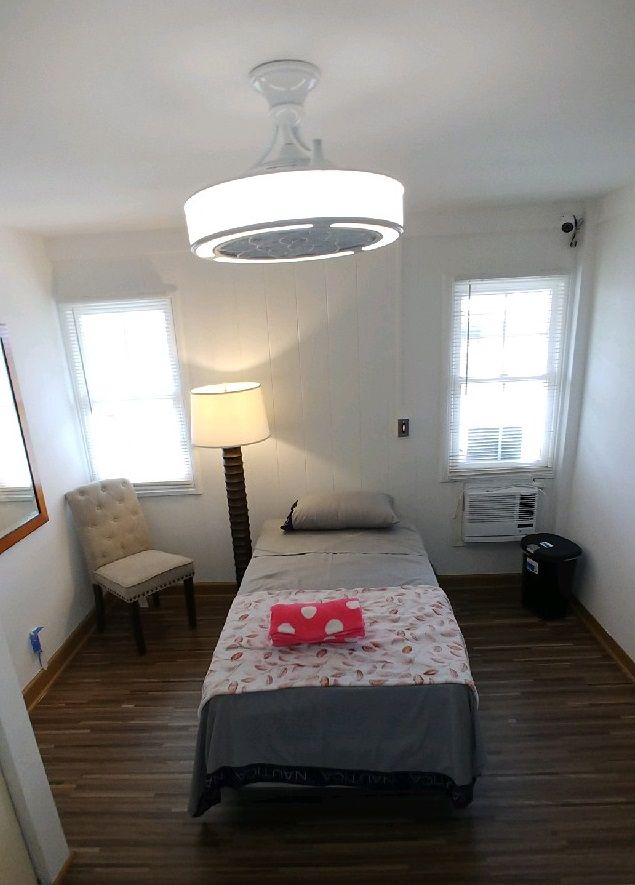 A minimalist bedroom with a single bed, lamp, and chair.