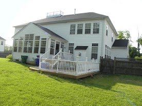 A two-story white house with a spacious backyard and a wooden deck.