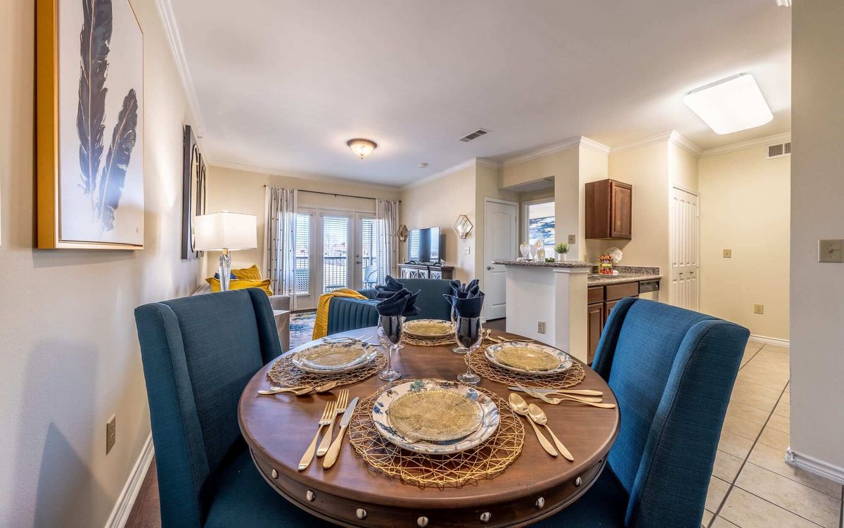 A modern dining area with a round table set for four, featuring elegant tableware and a stylish living space in the background.