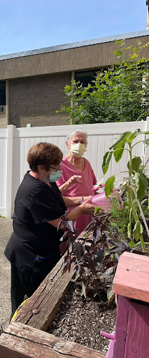 Two women tending to plants in a garden, both wearing masks.