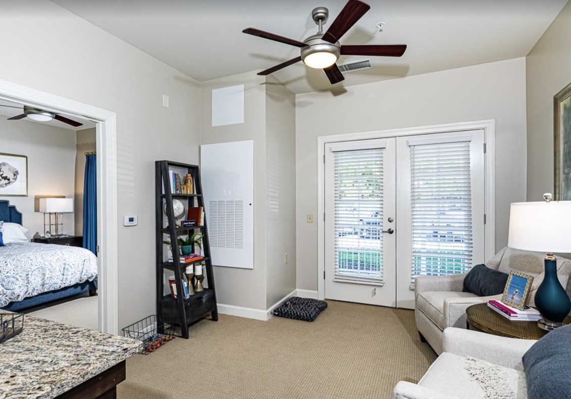 A cozy living room featuring a ceiling fan, bookshelf, and French doors leading outside.