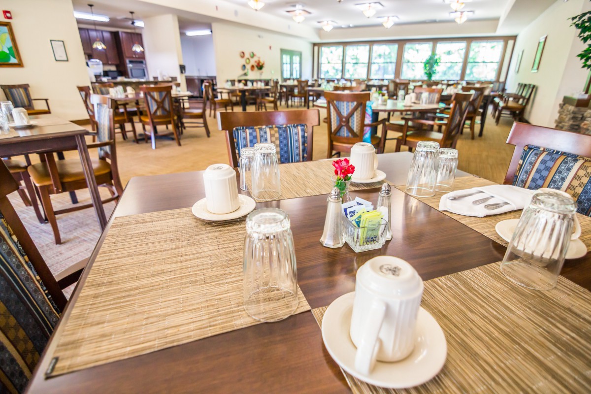 A spacious dining room with several tables neatly set with cups, glasses, and a flower centerpiece.