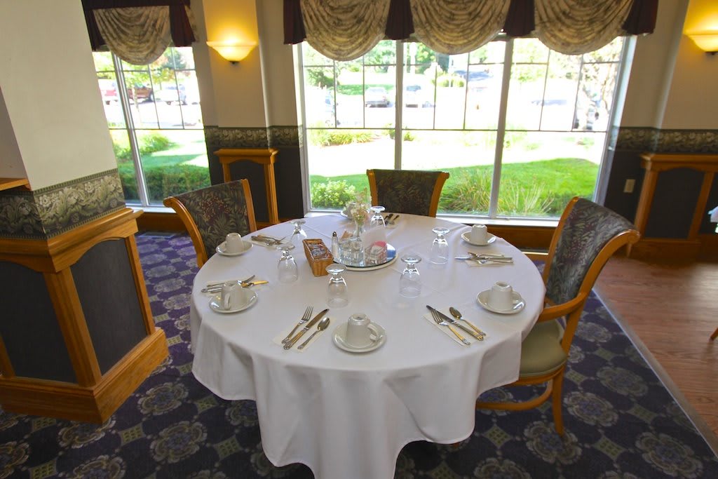 A elegantly set round table in a dining area with a view of the greenery outside.