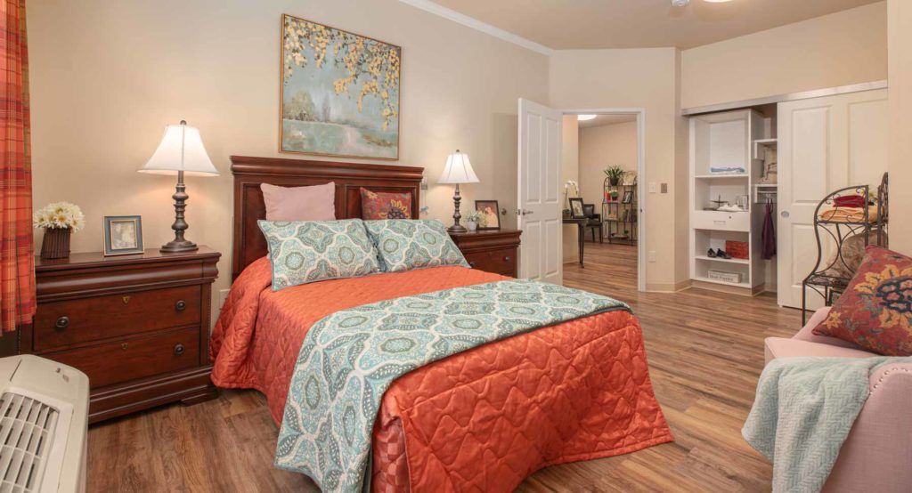 A cozy bedroom with a neatly made bed, featuring colorful bedding and decorative pillows.