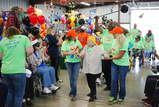 Volunteers assist elderly participants during a lively community celebration filled with colorful decorations and joyful energy.