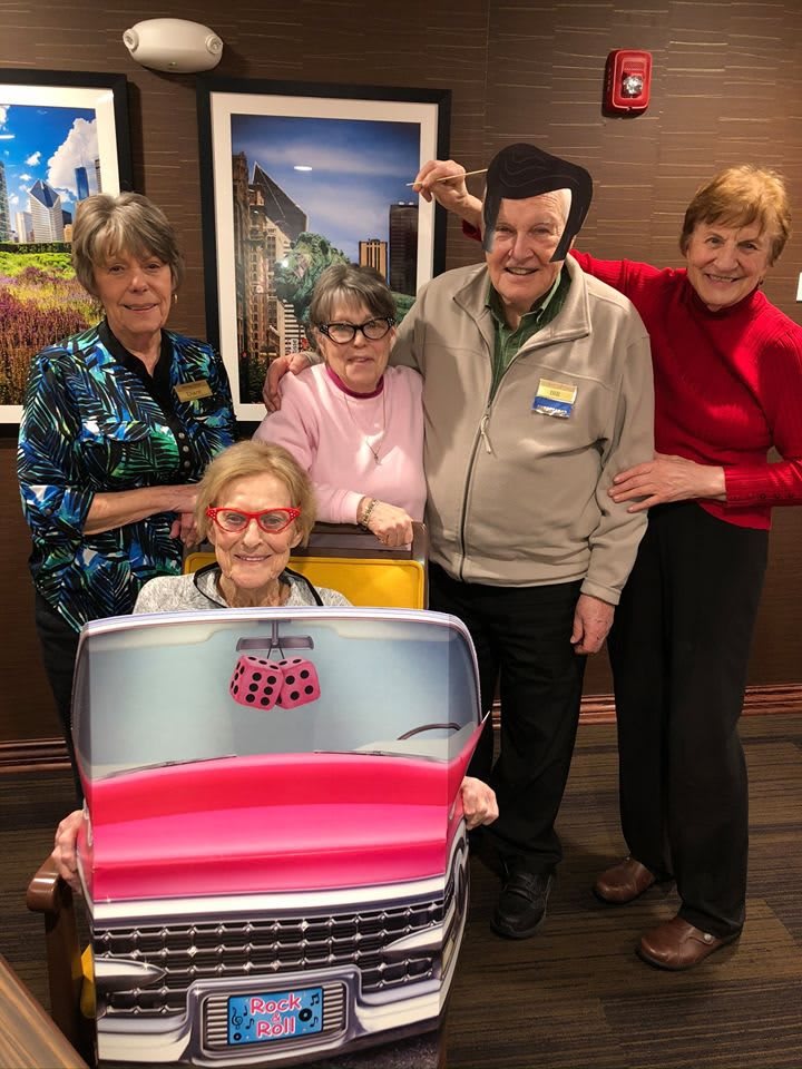 A group of seniors enjoying a fun activity together indoors, with one person in a car-themed costume.