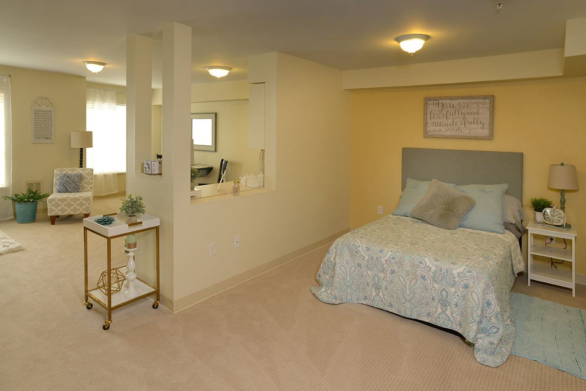 A cozy bedroom with a bed, decorative pillows, and a mirror reflecting the room's interior.