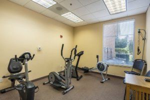 A small gym with various exercise equipment including a stationary bike, treadmill, and elliptical machine.