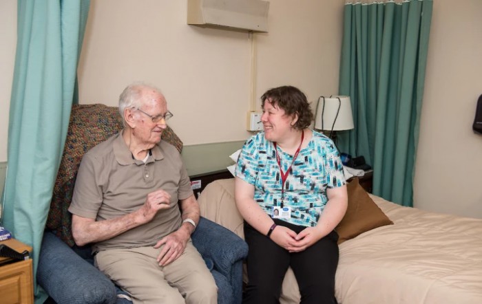 An elderly man and a caregiver having a conversation in a living room setting.