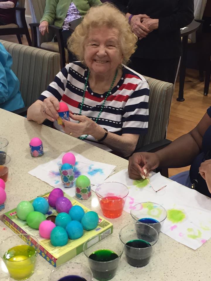 An elderly woman is happily decorating colorful eggs during a group crafting activity.